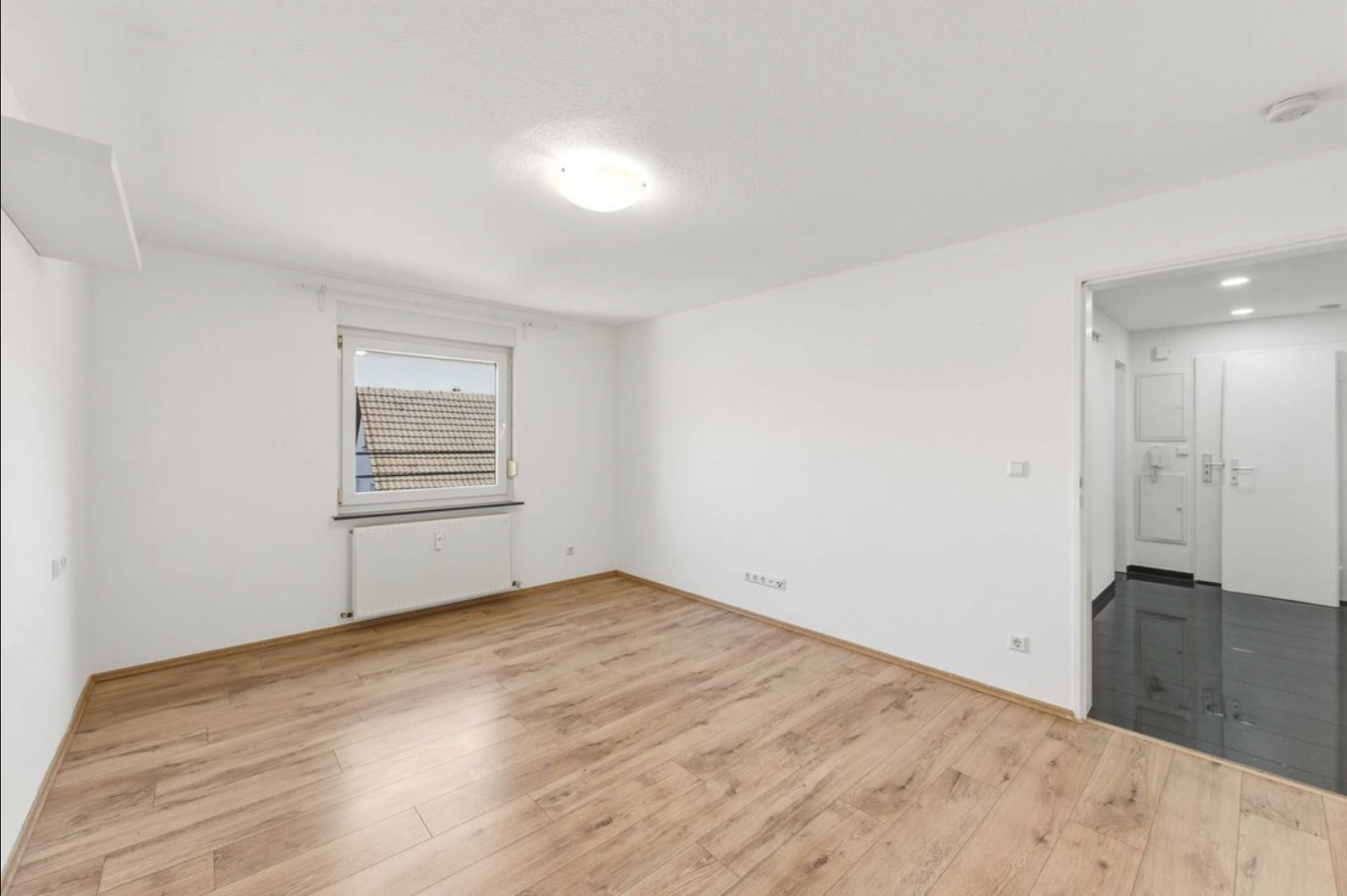 Bild einer leeren Wohnung mit Laminat in Holzoptik und Blick vom Zimmer zum Eingangsbereich